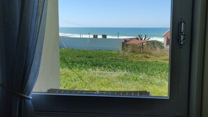 A window with a view of the ocean, a grassy area, and a building with a red roof. - Santa Cruz Ocean Apartment - II (Santa Cruz)