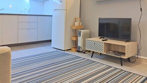A modern kitchen with white cabinets, a microwave, and a built-in oven. There is a white refrigerator, a wooden TV stand with a flat-screen TV, and a patterned rug on the floor. - Santa Cruz Ocean Apartment - II (Santa Cruz)