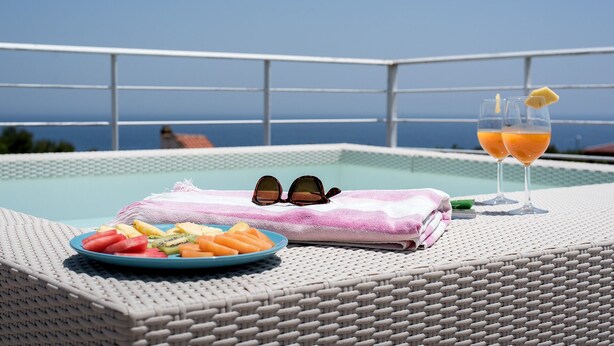 Ein Poolbereich mit Koransessel, Obstteller, Sonnenbrille und einem Glas Orangensaft.
