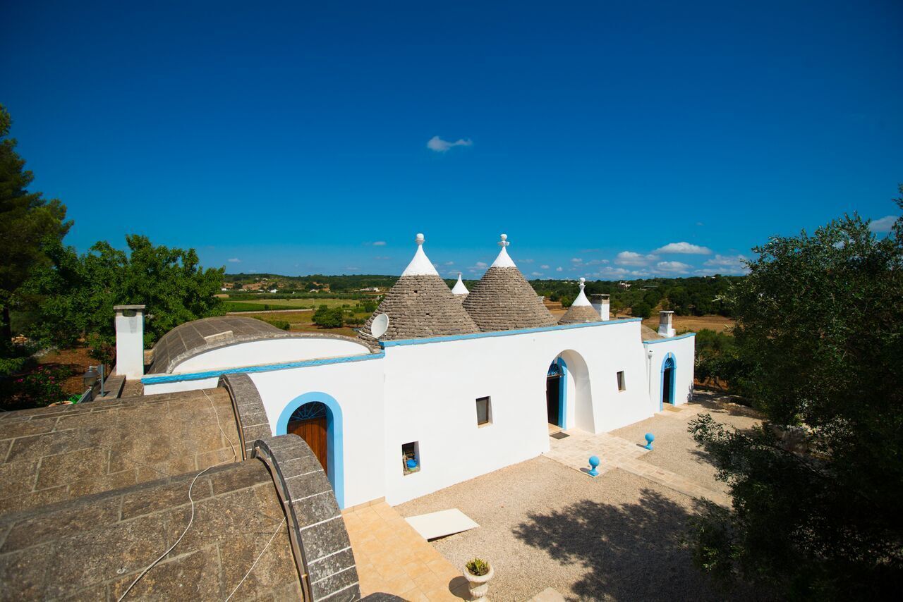 A white building with blue trim and multiple conical roofs, surrounded by greenery and a clear sky.