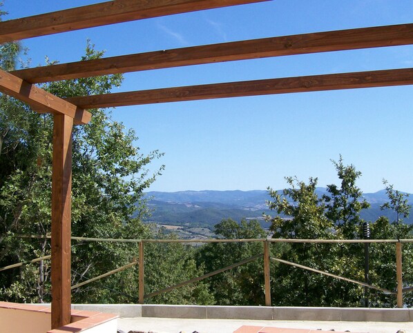 Une structure de pergola en bois offrant une vue sur les montagnes et les arbres au loin.
