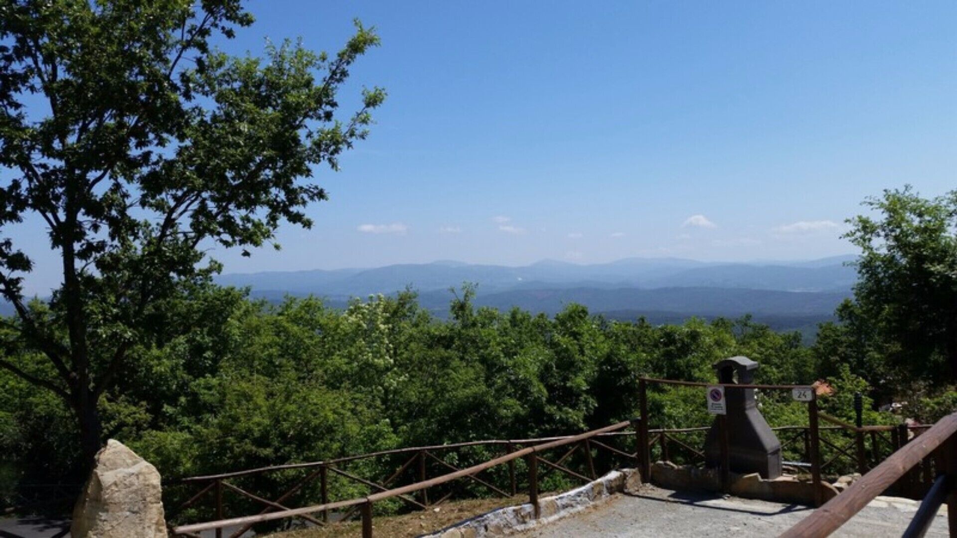 Um mirante panorâmico com guarda-corpo de metal e estrutura de pedra, com vista para uma paisagem montanhosa.