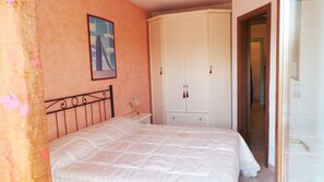 Une chambre à coucher comprenant un lit, une table de chevet, une armoire et une porte donnant sur une autre pièce.