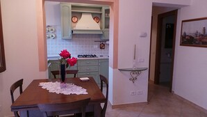 A dining area with a wooden table and chairs, a vase with flowers, and a kitchen in the background with light green cabinets and a tiled backsplash. - Horizons on the splendid Val di Cornia scenic two and comfortable  (Monteverdi Marittimo)
