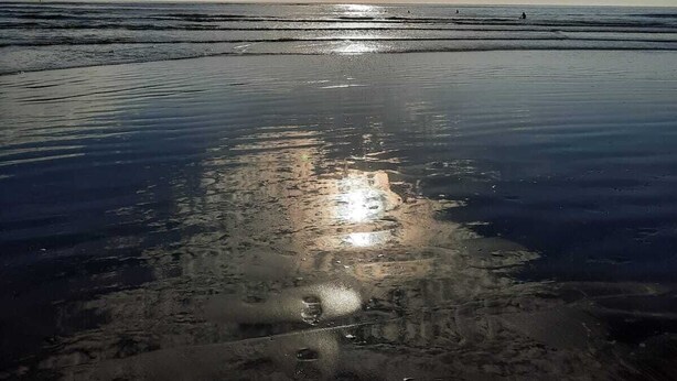 Una platja amb mar tranquil·la i un cel clar amb núvols.