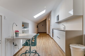 A narrow hallway with a kitchenette on the right, a white desk with a chair on the left, and a trash bin in the foreground. - Home Out Loft A - Loft at City Center (Lisboa)