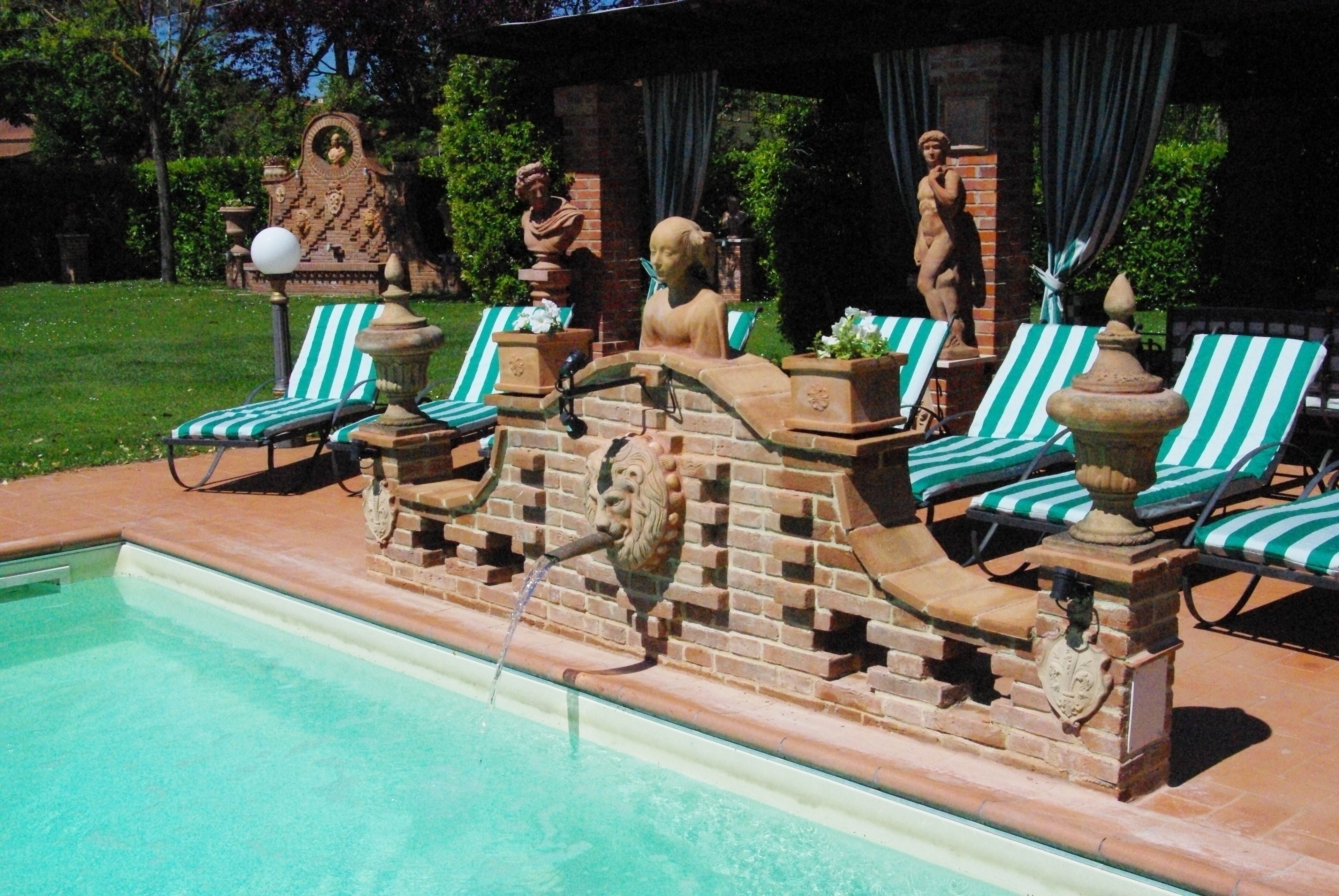 A poolside area with a brick wall, lounge chairs, and decorative statues.