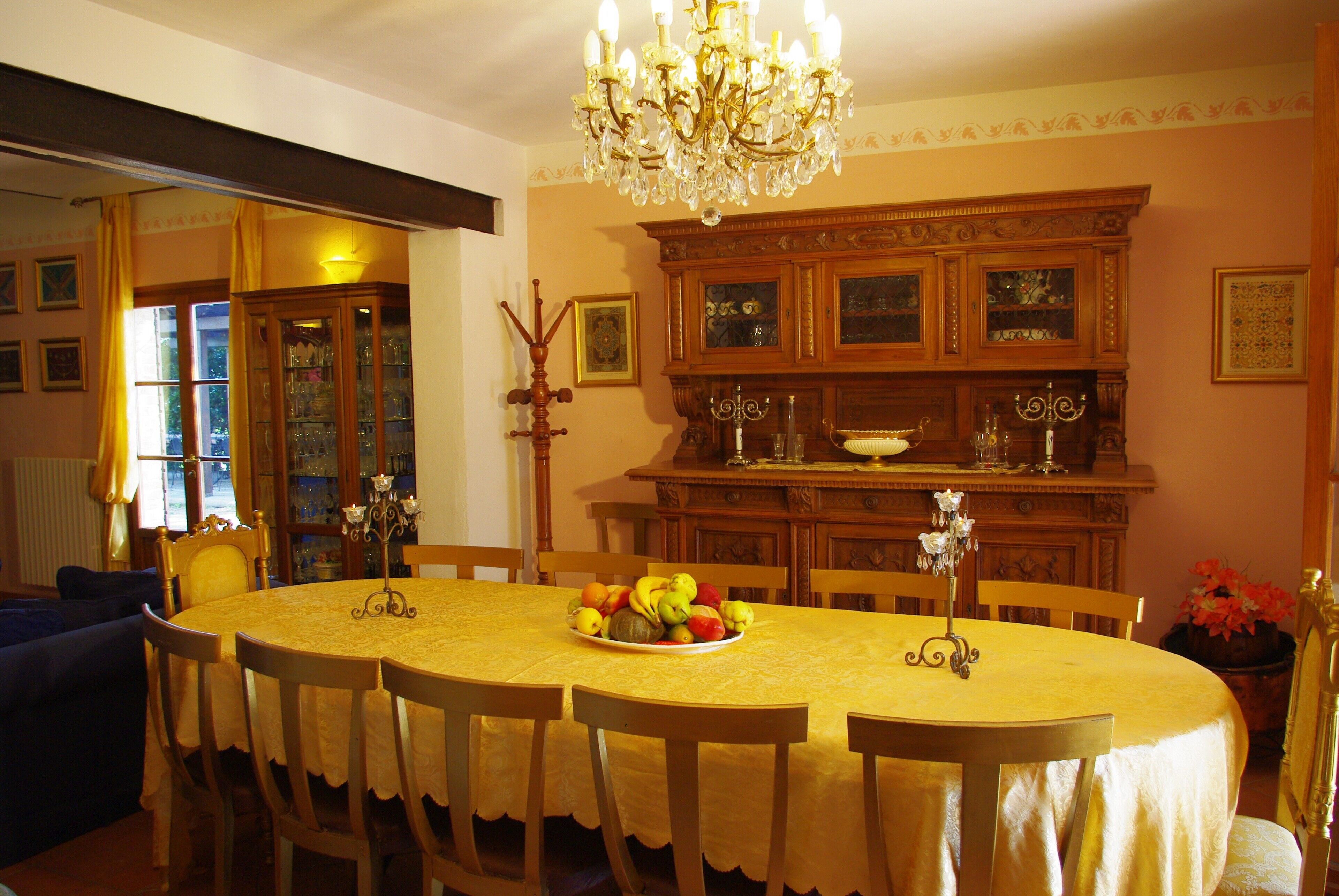 Comedor con una gran mesa ovalada, sillas, una araña y un aparador de madera con puertas de vidrio.