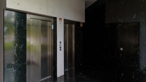 En moderne elevator med metaldoors og et kontrolpanel, placeret i en gang med mørke marmorvægge.