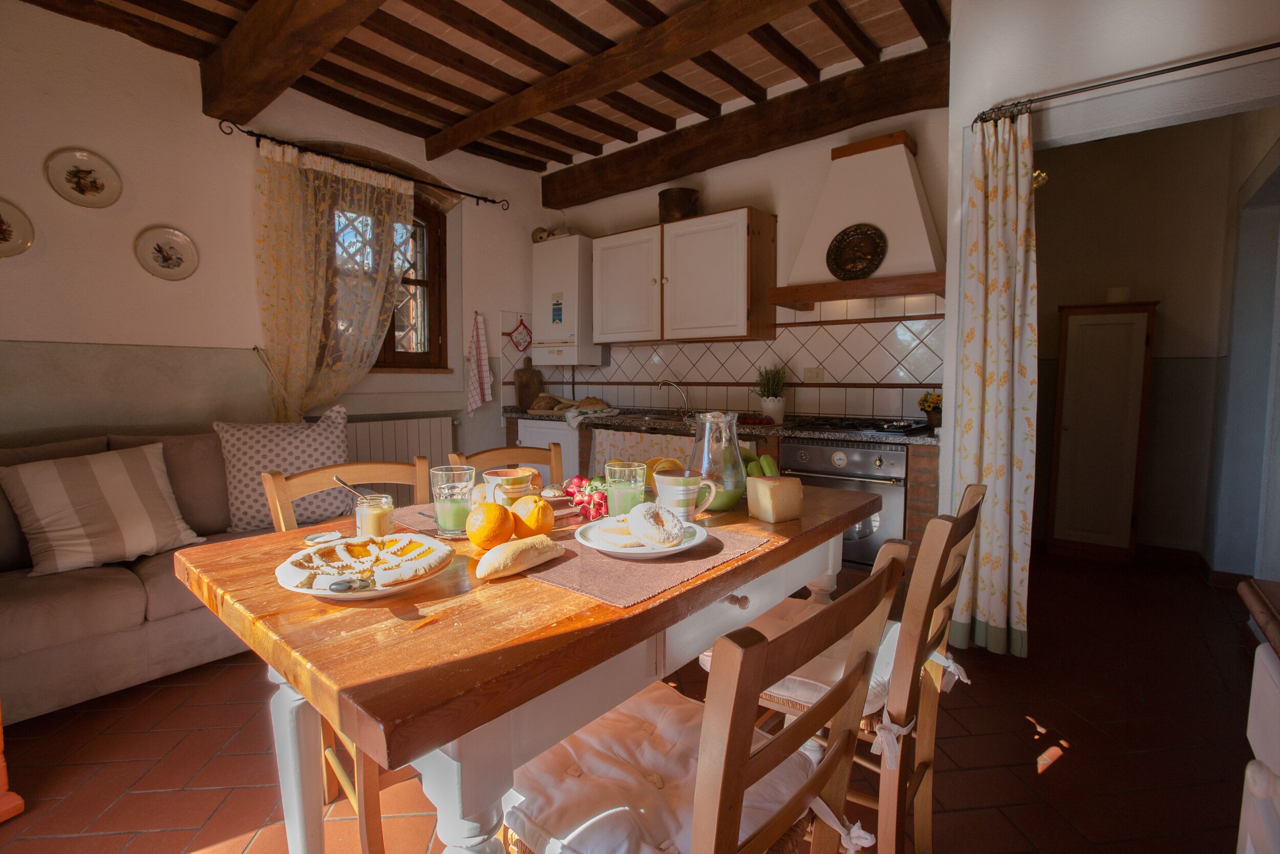 A cozy kitchen with a wooden table set for breakfast, a sofa, and a tiled backsplash.