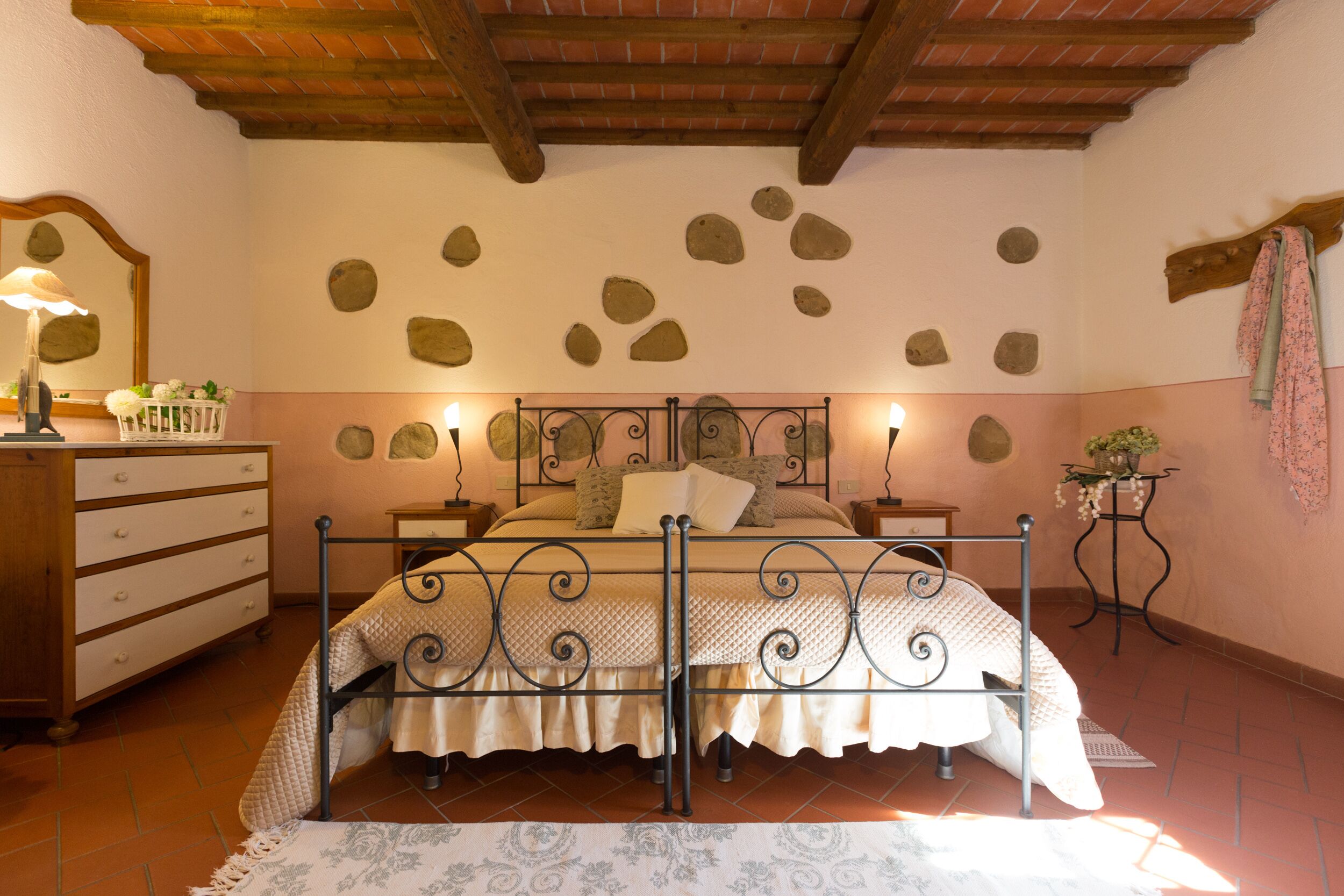 Een slaapkamer met een bed, een dressoir, nachtkastjes en een stenen muur.