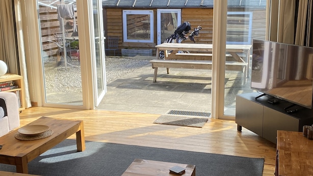 A modern interior with a wooden floor, a dining area, and a sliding glass door leading to an outdoor patio with a bicycle and a wooden building.