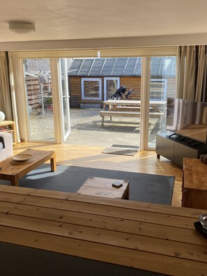 Un interior moderno con suelo de madera, zona de comedor y puerta corredera de vidrio que da a un patio exterior con bicicleta y construcción de madera.