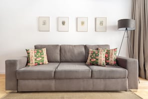A grey sofa with floral cushions, a floor lamp, and framed pictures on the wall. - Chiado | COMFY & EASY ACCESS | Family-Friendly (Lisboa)