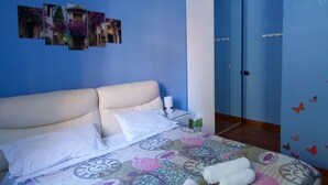 Une chambre à coucher comprenant un lit, des oreillers, une couvre-lit à motifs d’horloges, une table de chevet avec une lampe et une armoire.