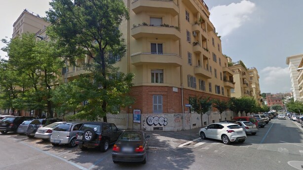 Un immeuble résidentiel à plusieurs étages, doté de balcons, avec des voitures garées et des arbres le long de la rue.