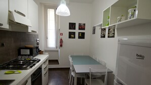 Une cuisine moderne avec des meubles blancs, une cuisinière à gaz, un réfrigérateur et un coin repas comprenant des chaises et une table.