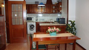 A compact kitchen with wooden cabinets, a washing machine, a microwave, and a dining table with a vase of flowers. - Artur apartment with balcony (Lousã)