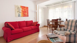 Een moderne woonkamer met een rode bank, een geruit fauteuil, een houten salontafel met tijdschriften, en een schaal met citroenen.