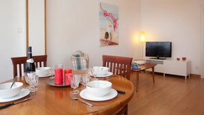 Een eethoek met een houten tafel gedekt voor vier personen, een televisie en een schilderij aan de muur.
