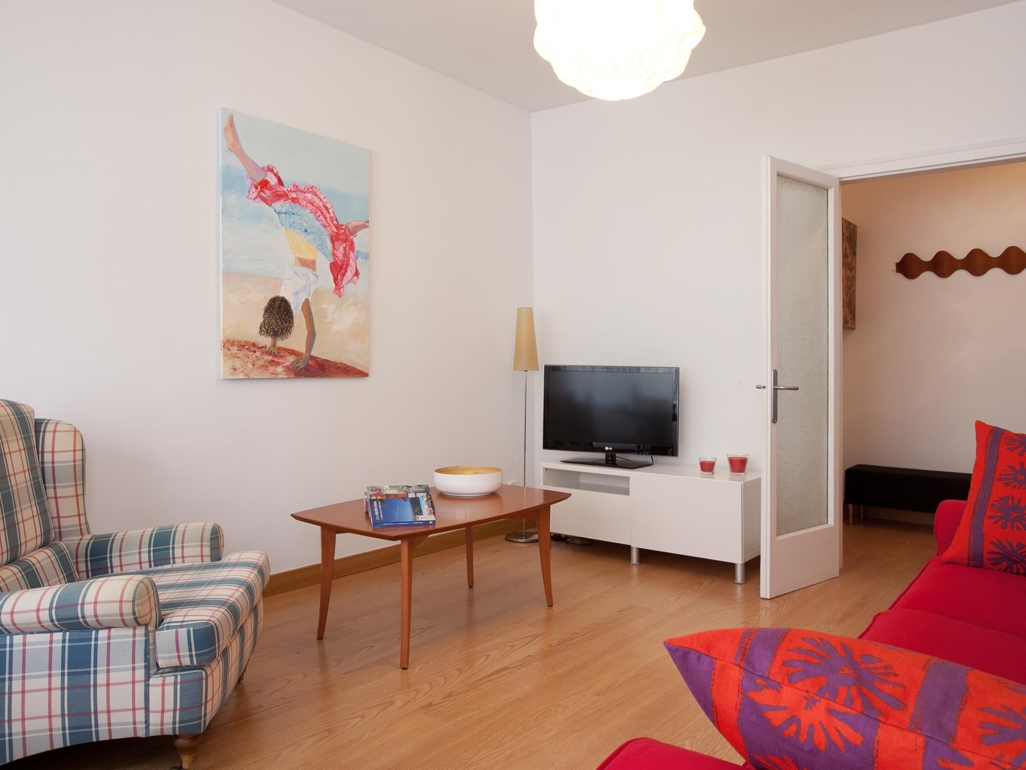 Ein Wohnzimmer mit einer Couch, einem Fernseher, einem Tisch und einem Bild an der Wand.