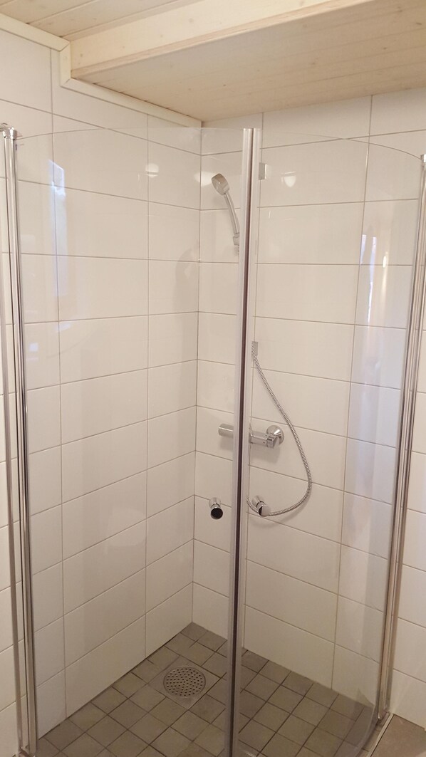A glass-enclosed shower stall with white tiled walls and a metal showerhead.