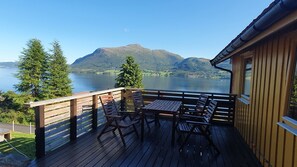 A wooden deck with a table and chairs overlooking a lake and mountains.