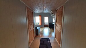 Un couloir étroit aux murs et au plancher en bois, qui mène à une pièce dotée d’un balcon.