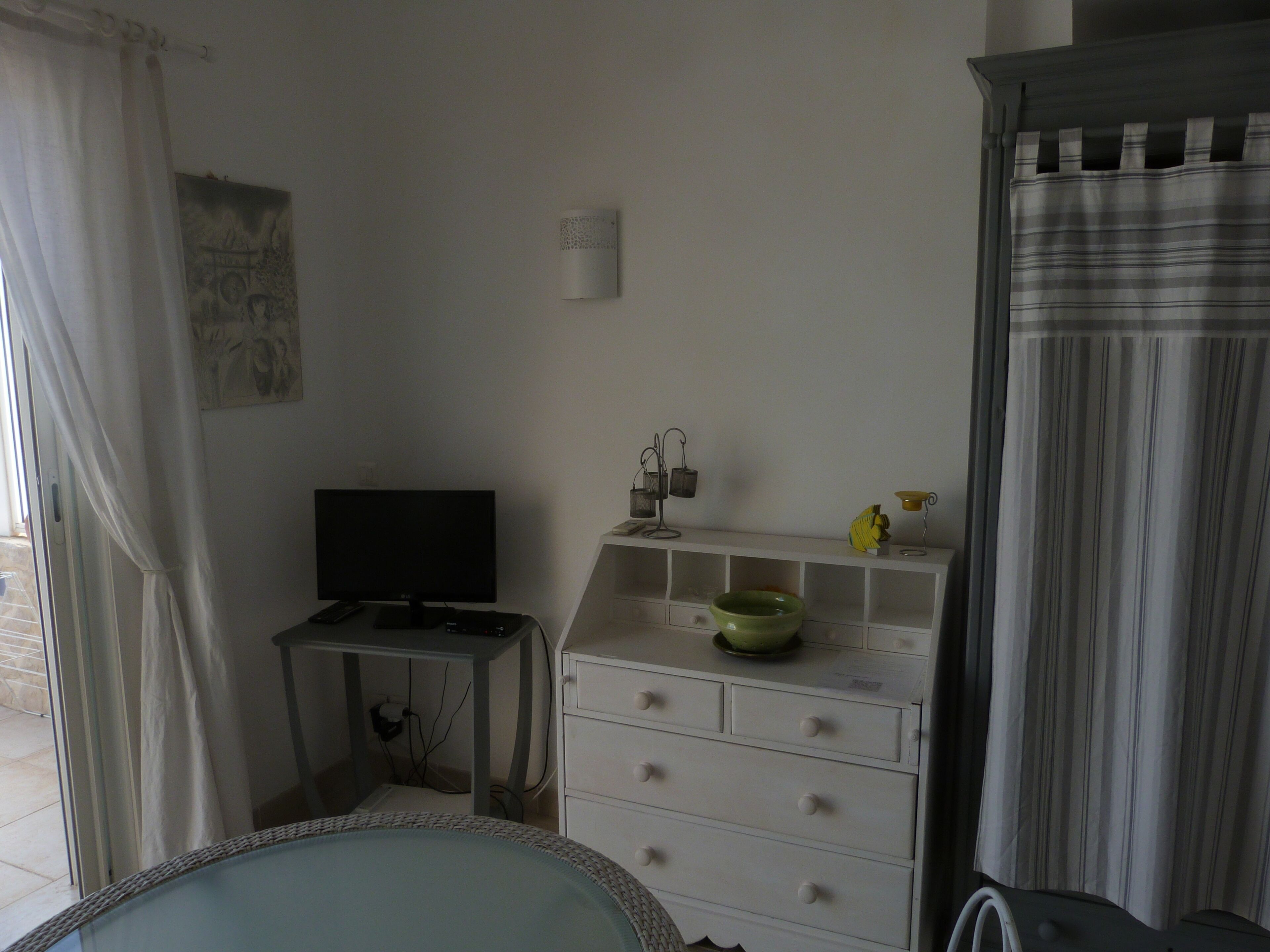 A bedroom with a bed, a desk with a computer, a dresser, and a window with curtains.