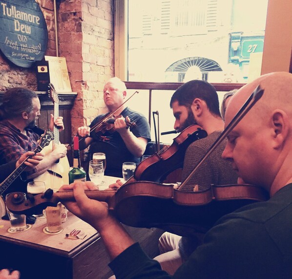 Un groupe de musiciens jouant d’instruments à cordes dans un cadre rustique, avec des murs en briques et une fenêtre en arrière-plan.