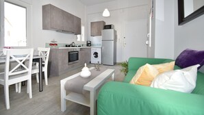 Ein kompakter Wohnbereich mit Küchenzeile, Essplatz und einem grünen Sofa mit Kissen.