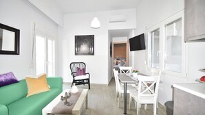 Ein modernes Wohnzimmer mit einem grünen Sofa, einem Esstisch mit weißen Stühlen, einem schwarzen Sessel mit weißem Kissen und einem flachbildfernseher, der an der Wand montiert ist.
