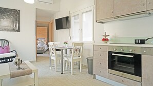 Eine moderne Küche mit weißen Schränken, ein Essbereich mit weißen Stühlen und ein Fernseher, der über der Arbeitsplatte angebracht ist.