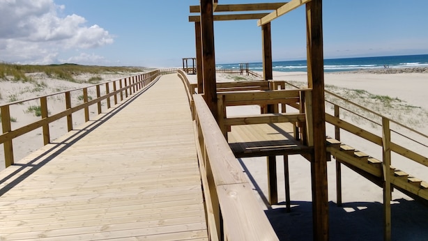 Une promenade en bois mène à une plage, et une structure en bois se trouve à son extrémité.