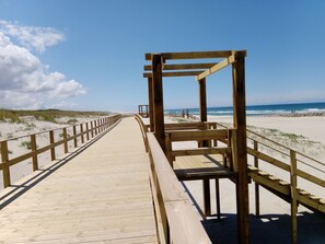 Une promenade en bois mène à une plage, et une structure en bois se trouve à son extrémité.