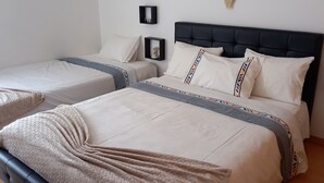Une chambre d’hôtel avec deux lits, chacun doté d’une tête de lit, de draps blancs et d’oreillers décoratifs. Des étagères murales accueillent de petits objets décoratifs.
