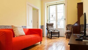 Un salon avec un canapé rouge, un fauteuil marron, une table basse en bois et un téléviseur.