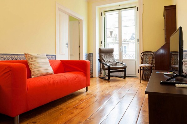 A living room with a red sofa, a brown armchair, a wooden coffee table, and a TV.