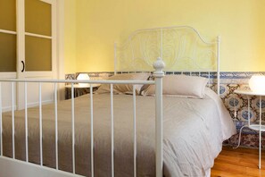 A bed with a white metal frame, beige bedding, and a nightstand with a lamp.