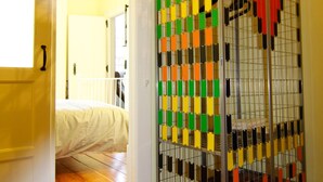 Une pièce avec un lit, une porte blanche et un objet rayé aux couleurs vives au premier plan.