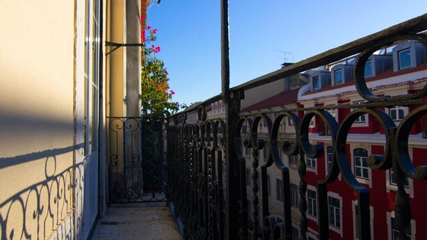 Une ruelle étroite, bordée d’une clôture en métal, et un immeuble aux façades rouge et blanche.