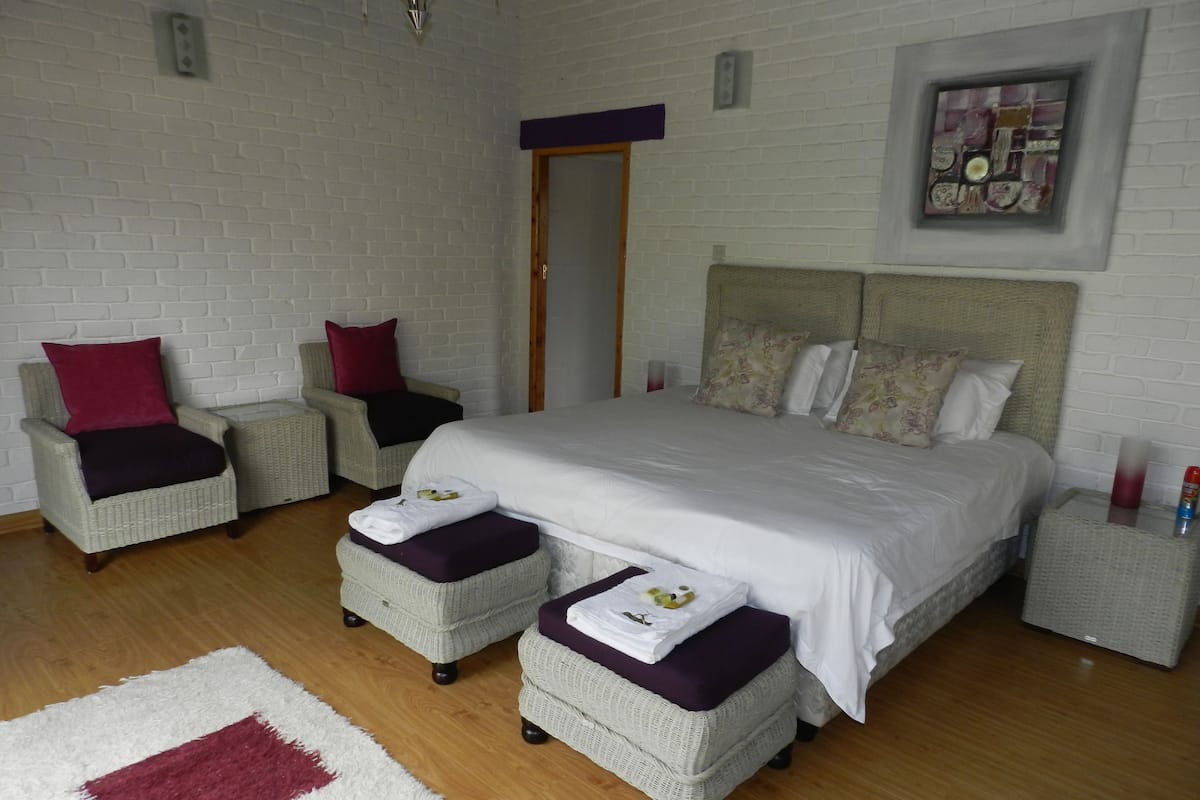 A bedroom with a large bed, two armchairs, a small table, and a nightstand.