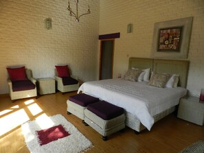 A bedroom with a large bed, two armchairs, a small table, and a nightstand. - Kutandara Lodges (Harare)