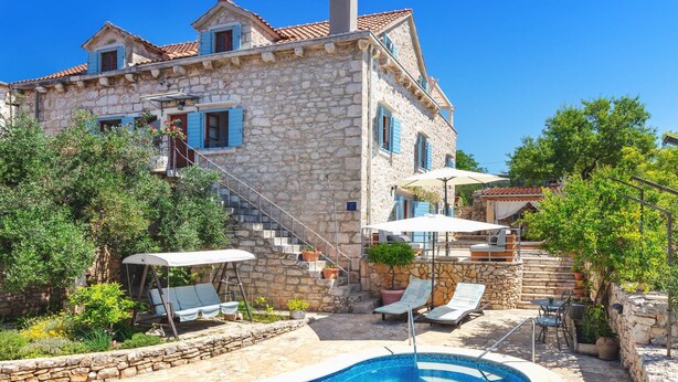 A stone villa with a swimming pool, outdoor seating, and a staircase leading to the upper floors.