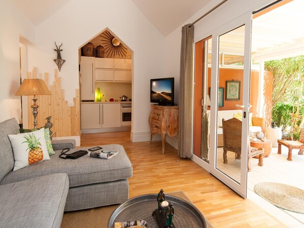 A modern living room with a grey sofa, a coffee table with decorative items, a television, and a sliding glass door leading to an outdoor area with furniture.