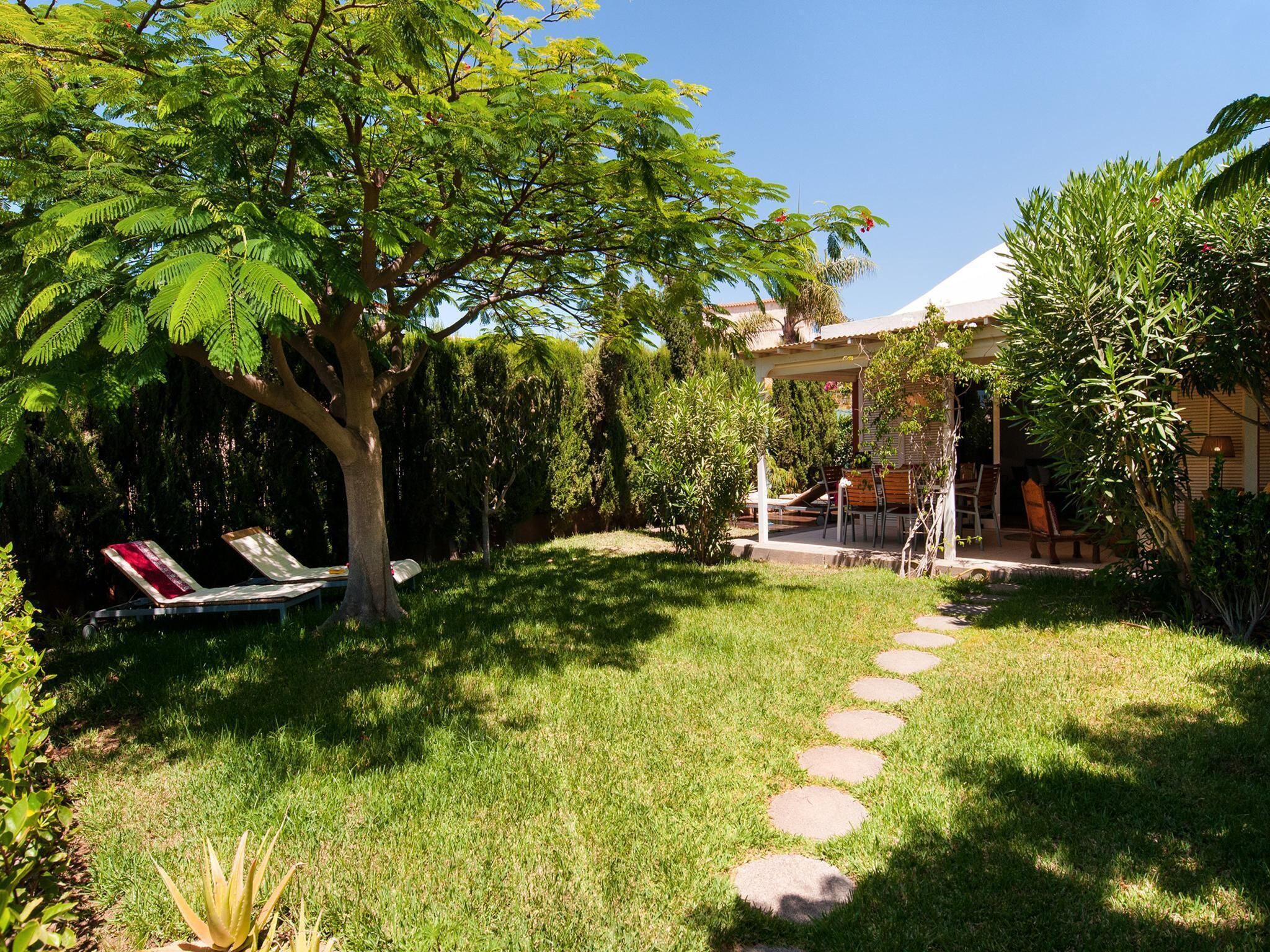 Ein gepflegter Garten mit Rasen, einer Pergola und einer Sitzecke mit Stühlen und einem Tisch.