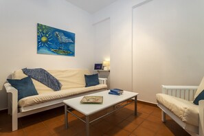 A living room with a white sofa, a coffee table, a painting on the wall, and a lamp.