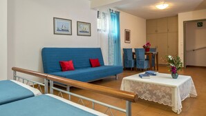 Una habitación con un sofá azul, una mesita con libros y una cama con cabecera de madera.