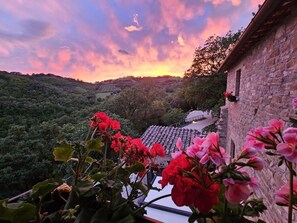 A view of a stone building with a tiled roof, surrounded by lush greenery and flowering plants. - APARTMENT: THREE-ROOM APARTMENT INSIDE AN ANCIENT CASTLE WITH PANORAMIC POOL (Perugia)