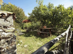 A rustic outdoor setting with a stone wall, a wooden bench, a picnic table, and a red umbrella.